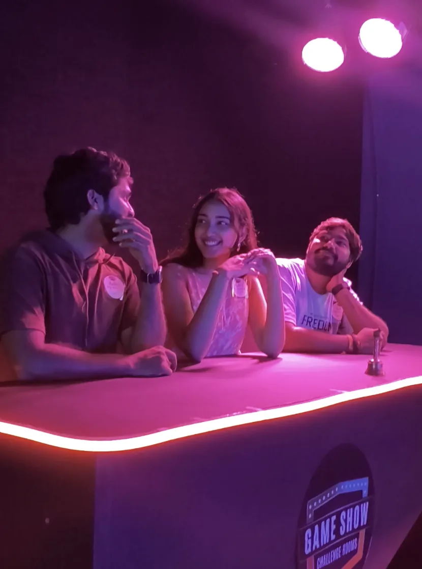 Three players at the buzzer desk under pink lights